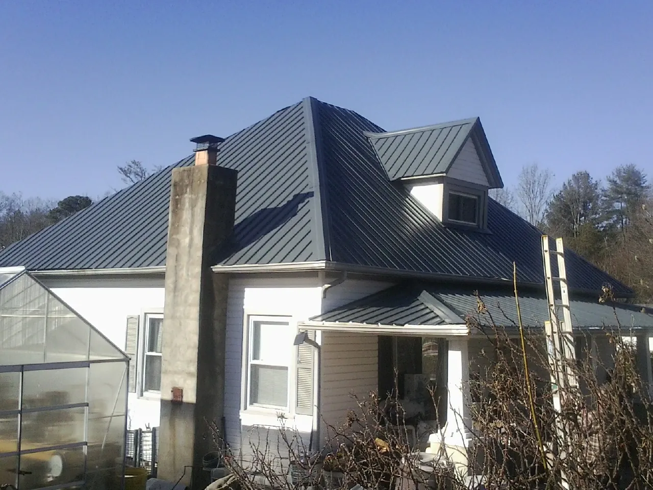Dark blue standing seam metal roof on a white farmhouse with dormer — Slate & Tile Roof Repair by Roofing Brothers in Leota