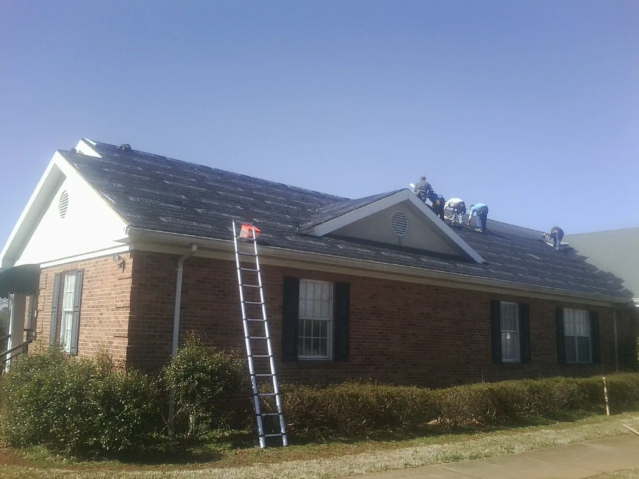 Crew tearing shingles off a brick ranch roof with a ladder set — Metal Roof Repair work by our crew in Leota
