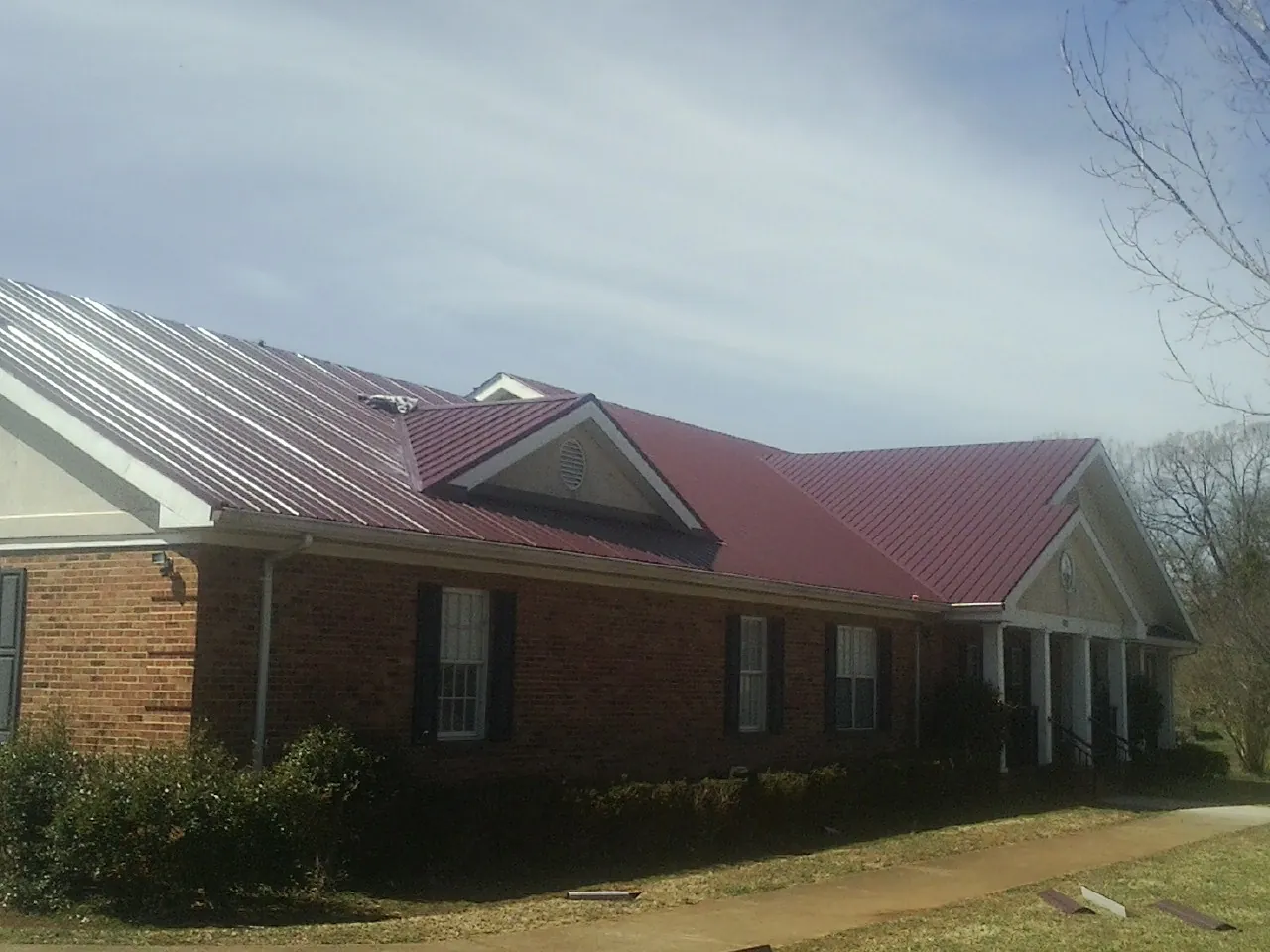 Red metal roof with gabled entries on a long brick building, from a Hail Damage Roof Repair job in Leota