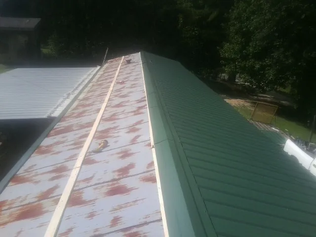 Old rusted panels beside newly installed green metal roofing — Wind Damage Roof Repair by Roofing Brothers in Leota