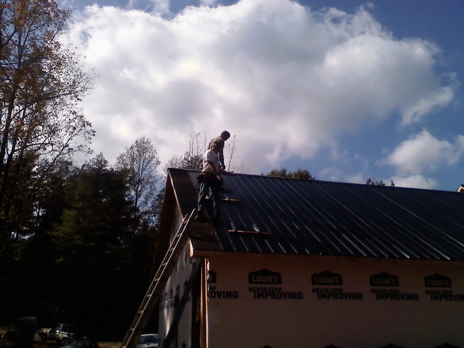 Roofer fastening dark metal panels high against a cloudy sky, from a Roof Inspection job in Leota