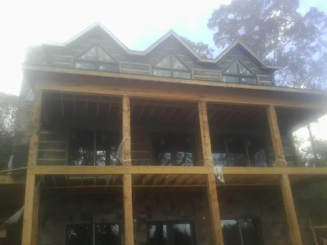 Dormers and porch framing on a large log home under construction — Roof Coating work by our crew in Leota