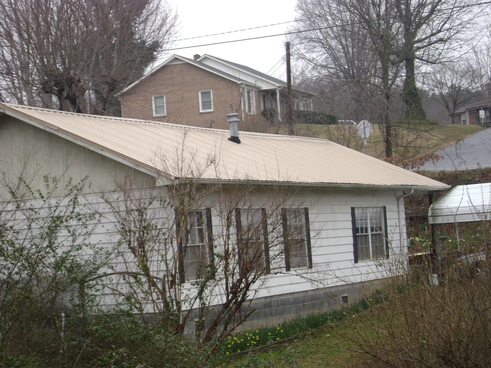 Tan metal roof on a white sided house set into a hillside — Commercial Roofing by Roofing Brothers in Leota