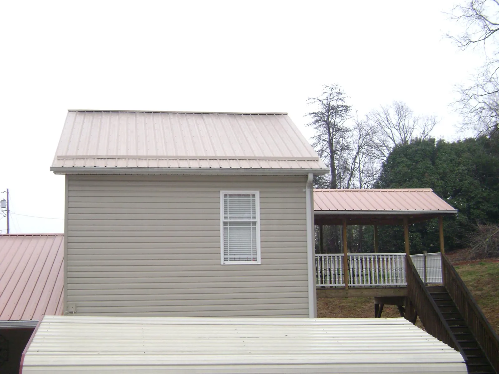 Tan metal roofs on a two story addition and attached porch, from a Roof Replacement job in Leota